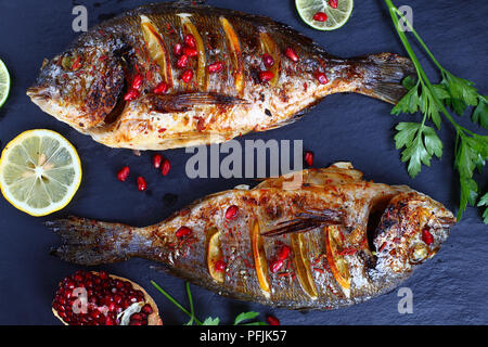 Gegrillter Fisch mit frischem Zitrus, Kräuter Gewürze und Granatapfel Samen auf dunklem Schiefer Fach, Ansicht von oben, close-up Stockfoto