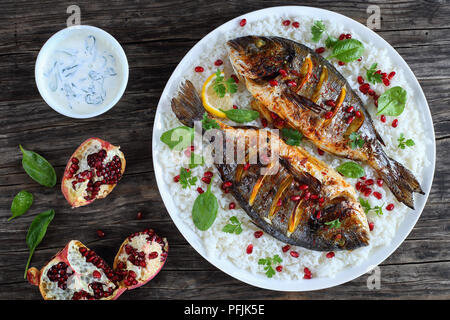 Gegrillter Fisch mit frischem Zitrus, Kräuter Gewürze und Granatapfel Samen serviert mit Reis, weißer Teller Spinat mit Sahne Soße auf alten, dunklen Stockfoto