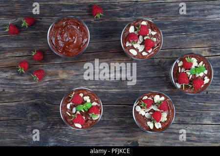 Köstliche Schokoladenmousse im Glas Tassen mit Minze, frische Himbeeren und Mandelflocken auf alten, dunklen Holztisch eingerichtet, klassische französische Cuis Stockfoto