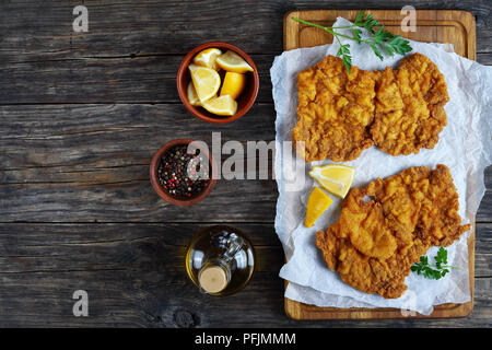 Köstliche Golden Brown zwei Wiener Schnitzel aus Kalbfleisch, Scheiben, Schmetterlingsflügel ausschneiden, auf Schneidebrett mit Zitrone und Petersilie serviert, Auth Stockfoto