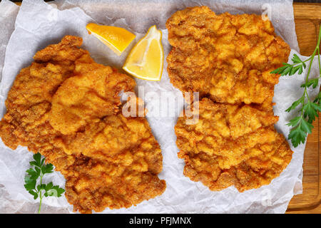 Köstliche Golden Brown zwei Wiener Schnitzel aus Kalbfleisch, Scheiben, Schmetterlingsflügel ausschneiden, auf Schneidebrett mit Zitrone und Petersilie serviert, Auth Stockfoto