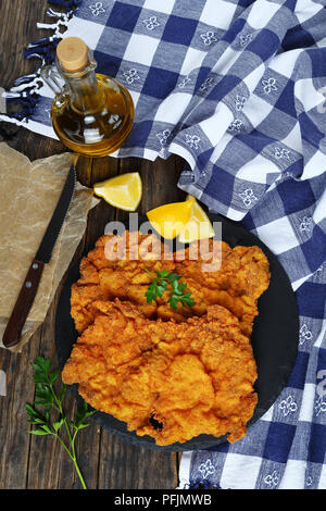 Köstliche Golden Brown zwei Wiener Schnitzel aus Kalbfleisch, Scheiben, Schmetterlingsflügel ausschneiden, auf schwarzen Stein Teller serviert, Küchentuch, Olivenöl, knif Stockfoto