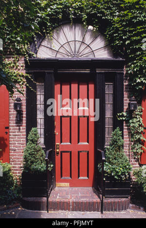 USA, New York, Detail der Fassade mit Tür, Rot, Holz- Tür mit Glas und schwarzen Türrahmen, von Ivy umgeben, in der Nähe. Stockfoto