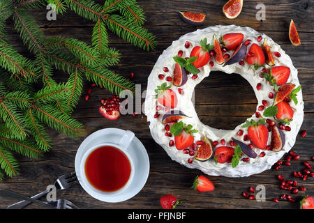 Köstliche pavlova Kuchen Kranz der französischen Baiser und Sahne, dekoriert mit Erdbeere, Feigen, Granatapfel und Minze auf dunklen Tisch mit Weihnachten Stockfoto