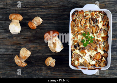 Köstliche würziger Eintopf mit Pilzen und saurer Sahne Sauce Auflaufform auf alten Brettern mit Steinpilzen auf Hintergrund, horizontale Ansicht her Stockfoto