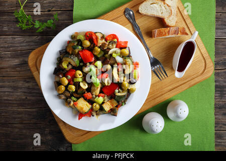 Gedünstetem Gemüse mit Aubergine, grünen Oliven, Kapern, Sellerie und Kräutern auf einem weissen Teller, Ansicht von oben Stockfoto