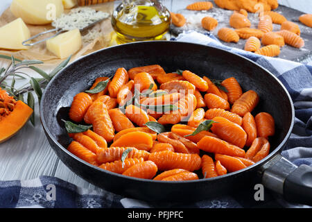 Appetitlich Kürbis Gnocchi in Butter gebraten mit frischen Salbeiblätter in einer Pfanne, auf Küchenpapier. geriebener Käse, Pin, Rohteig und roher gnocch Stockfoto