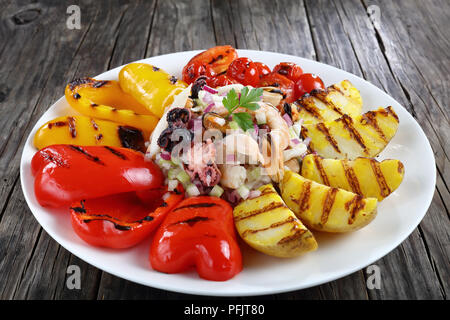 Lecker Salat mit Garnelen, Tintenfisch, Tintenfisch, Miesmuscheln serviert mit gegrilltem Gemüse auf weiße Platte auf dunklen Holztisch, Ansicht von oben, close-up Stockfoto