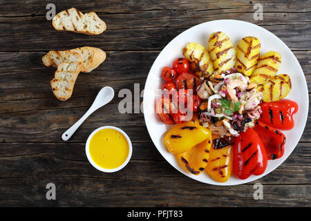 Lecker spicy Seafood Salat beträufelt mit Zitronensaft serviert auf weiße Platte mit gegrilltem Gemüse. basic rue Sauce und geröstetem Baguette auf Holz Stockfoto