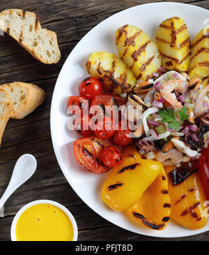 Leckeren, gesunden Fisch Salat beträufelt mit Zitronensaft serviert auf weiße Platte mit gegrilltem Gemüse. basic rue Sauce und geröstetem Baguette auf Woode Stockfoto