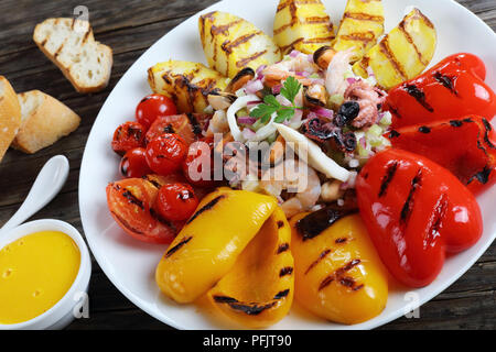 Leckere gemischte Meeresfrüchte Salat serviert auf weiße Platte mit gegrilltem Gemüse. basic rue Sauce und geröstetem Baguette auf Holztisch, horizontale close-u Stockfoto