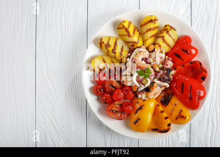 Garnelen, Tintenfisch, Tintenfisch, Muscheln und Meeresfrüchte Salat mit gegrilltem Gemüse auf weiße Platte auf hölzernen Tisch serviert, leeren Raum für Text, Ansicht von links Stockfoto