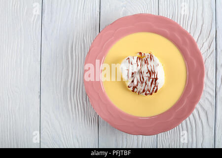 Eine schwimmende Insel Dessert oder Vögel Milch, bestehend aus Baiser schwimmend auf Creme Anglaise und mit Ganache in einem rosa Platte beträufelt, Aussicht f Stockfoto