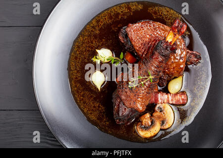 Ein Teil von Coq au Vin - klassische französische Eintopf, in dem Huhn langsam in Rotwein mit Kräutern, Pilzen und Gemüse geschmort ist, serviert. Stockfoto