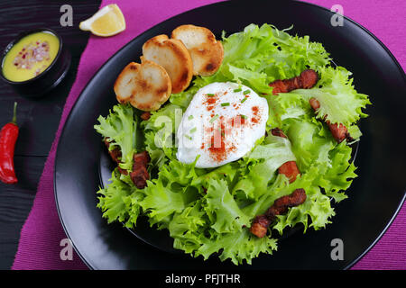 Ein traditionelles Lyonnaise Salat, aus frisee Eisbergsalat, in einem warmen und leckeren Vinaigrette geworfen und gekrönt mit knusprigem Speck und ein pochiertes Ei, Serv Stockfoto