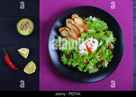 Ein traditionelles Lyonnaise Salat, aus frisee Eisbergsalat, in einem warmen und leckeren Vinaigrette geworfen und gekrönt mit knusprigem Speck und ein pochiertes Ei, Serv Stockfoto