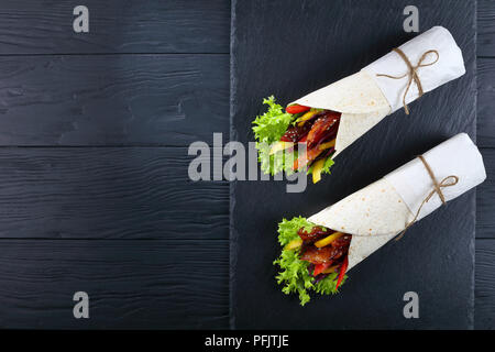 Köstliche frisch zubereitete sandwich Wraps mit frisee Eisbergsalat, Paprika, Krautsalat und Fried Chicken Sticks auf schwarzen Stein Fach, von oben betrachten Stockfoto