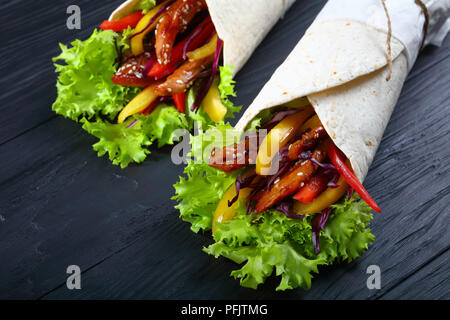 In der Nähe von köstlichen frischen saftigen Fladenbrot sandwich Wraps mit frisee Salat Gemüse Salat und gebratene spicy Chicken Filet auf schwarzen Brettern Stockfoto