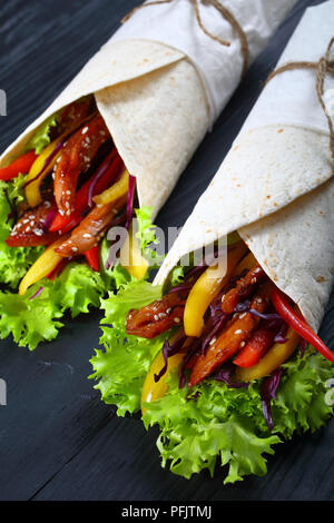 In der Nähe von zwei köstlichen frischen saftigen Fladenbrot shawarma Wraps mit frisee Salat, Gemüse und gebraten würzige Hähnchenfilet auf schwarzen Brettern, Stockfoto