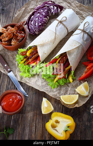 In der Nähe von zwei köstlichen frischen saftigen Fladenbrot shawarma Wraps mit frisee Salat, Gemüse und gebraten würzige Hähnchenfilet auf Papier, Zutaten für ein Stockfoto