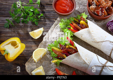 Köstlich frischen saftigen Fladenbrot shawarma Wraps mit frisee Salat, Gemüse und gebraten würzige Hähnchenfilet auf Papier, Zutaten und Tomatensauce ein Stockfoto
