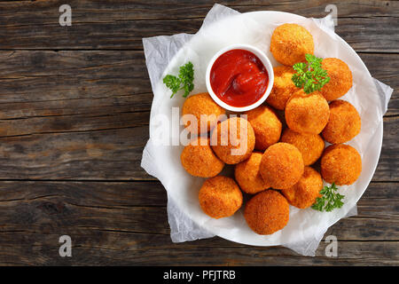 Kroketten - kartoffelpüree Kugeln paniert und frittiert, serviert mit Tomatensoße auf die Platte an der alten, dunklen Holztisch, Ansicht von oben Stockfoto