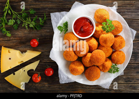 Kroketten - kartoffelpüree Kugeln paniert und frittiert, serviert mit Ketchup auf die Platte an der alten, dunklen Holztisch mit Tomaten und Käse Slice Stockfoto