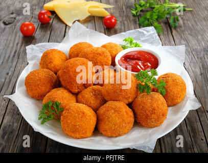 Kroketten - kartoffelpüree Kugeln paniert und frittiert, serviert mit Ketchup auf die Platte an der alten, dunklen Holztisch mit Tomaten und Käse Slice Stockfoto