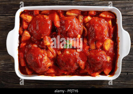 Close-up lecker Fleischbällchen gebacken in Tomatensauce mit Karotten, Pastinaken und Zwiebel in eine Auflaufform auf rustikalen Holztisch, Ansicht von oben Stockfoto