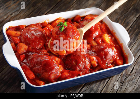 Nahaufnahme der Löffel aus Holz mit einem Türkei Meatball in Tomatensoße und Gemüse geschmorte in einer Auflaufform, Ansicht von oben Stockfoto