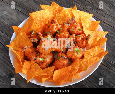 Nahaufnahme der leckere Chicken Wing Lutscher mit Mais nachos auf einem weißen Teller auf dunklen Holz- Tabelle, Ansicht von oben Stockfoto