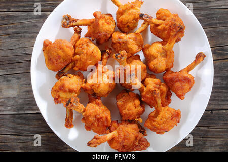 Leckere frittierte Zerschlagene knusperiges Huhn Winglets auf einem weißen Teller auf dunklen Holztisch, horizontale Ansicht von oben Stockfoto