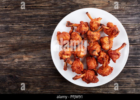 Leckere frittierte Zerschlagene crispy Chicken Wings mit freiliegenden Knochen auf eine weisse Platte auf dunklen Holztisch, horizontale Ansicht von oben, Copyspace lef Stockfoto
