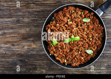 Bolognese Sauce - Hot Juicy Rinderhackfleisch geschmort mit Tomatensauce, Gewürze, Basilikum, fein gehackt Gemüse und Sellerie in Skillet auf Holztisch, Auth Stockfoto