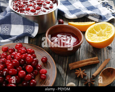 Cranberry Sauce in Topf und Schüssel auf hölzernen Tisch mit frischen Cranberry auf Platte und Zutaten auf Hintergrund, authentische Rezept, horizontale Ansicht Stockfoto