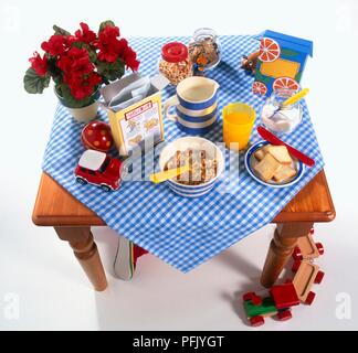 Frühstück und Spielzeug auf Holztisch mit karierten Tischdecken, Fuß des Kindes unter Tabelle Stockfoto