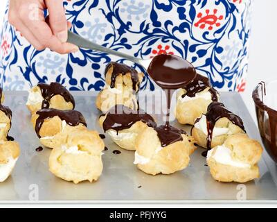 Gießen von Schokolade über Profiteroles auf Backblech, mit Löffel, close-up Stockfoto