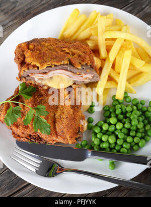 Lecker Schnitzel Cordon Blue mit Pommes frites, Erbsen und Petersilie auf die Platte an der alten, dunklen Holztisch, authentische Rezept, Ansicht von oben, close-up Stockfoto