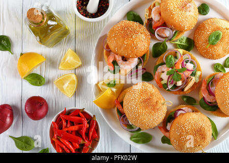 Leckere Burger oder pinchos mit Meeresfrüchte - Krabben, Muscheln, Tintenfisch Streifen, roten Zwiebeln und Spinat auf weißem Teller,; Zitronenscheiben, marinierte Paprika auf Holz Stockfoto