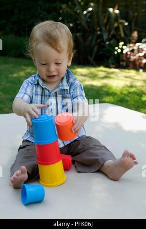 Baby Junge sitzt auf der Decke im Garten spielen mit Plastikbechern stack, close-up Stockfoto