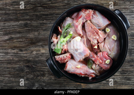 Stück Kaninchen roh mariniert mit Weißwein, Knoblauch, Gewürze und Bündel von aromatischen Kräutern oder bouquet garni in schwarz Auflaufform, Ansicht von oben Stockfoto