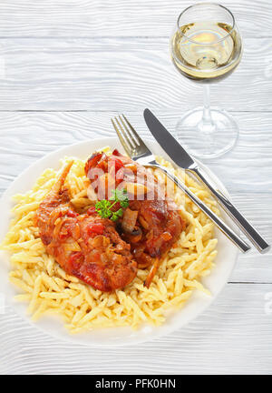 Köstliches Kaninchen Beine geschmort mit Gemüse und Kräutern, serviert mit italienischer Pasta auf weiße Platte mit einem Glas Weißwein auf Holztisch, gesund re Stockfoto