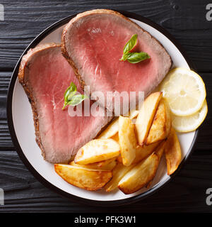Beef Steak mit Bratkartoffeln und Zitrone in der Nähe serviert auf einem Teller auf einem Schwarzen Tisch. nach oben Ansicht von oben Stockfoto