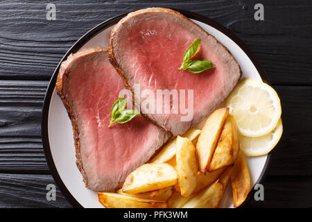 Saftig gegrilltes Rindersteak mit Bratkartoffeln und Zitrone close-up auf einem Teller auf dem Tisch. horizontal oben Ansicht von oben Stockfoto