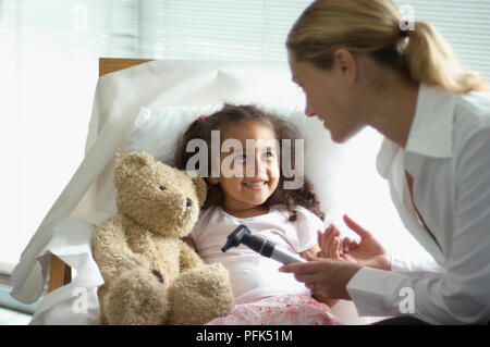 Ärztin holding Otoskop über Mädchen im Bett Stockfoto