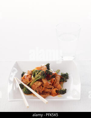 Huhn unter Rühren braten mit Broccoli und Nudeln, Essstäbchen auf die Kante der Platte, und Glas Wasser Stockfoto