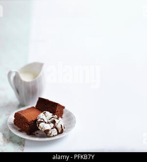 Chocolate brownies und eine Schokolade crinkle Cookie auf einem Teller, mit einer Kanne Creme in der Nähe, close-up Stockfoto