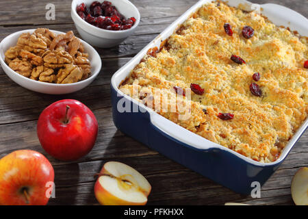 Close-up von leckeren Apfelkuchen oder Apple Crisp in Auflaufform mit Zutaten auf dunklen Holztisch, gesund und einfach im Winter Frühstück Rezept, hor Stockfoto