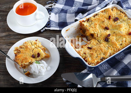 Lecker Apple Crumble oder Apple Crisp in Auflaufform und ein Teil auf der Platte mit hausgemachten Kokosmilch Eis. Tasse Tee im Hintergrund, Blick von Stockfoto