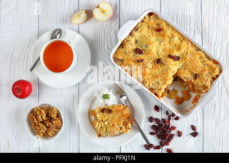 Frühstück - Apple Crumble oder Apple Crisp in Auflaufform und ein Teil auf Platte mit Kokosmilch und Tasse Tee auf Tabelle, Ansicht von oben, Clos Stockfoto